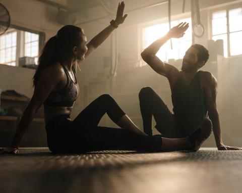 A woman and man sitting on the gym floor, high-fiving each other. 